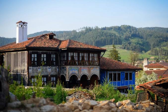 A painted 19th-century house with red tile roofs in Koprivshtitsa, green hills behind